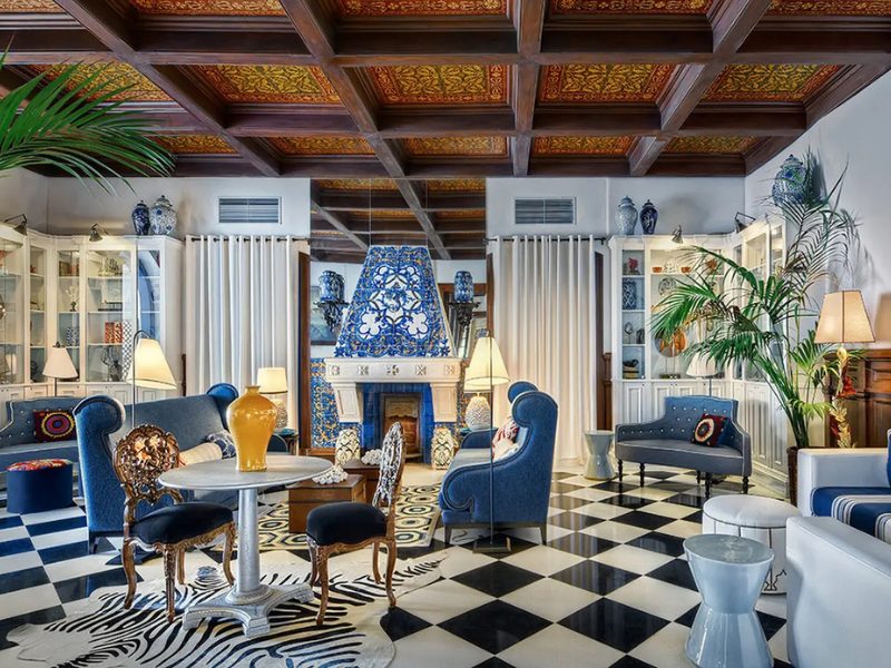 A richly decorated living room with blue velvet furniture, a black and white checkered floor, a zebra rug, and a fireplace with blue and white tiles.