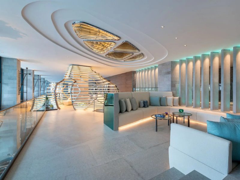 A modern lounge area with a curved sofa, decorative ceiling lights, and a unique sculptural structure.